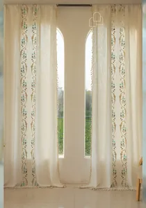 Détail d'un rideau en lin crème avec broderie florale bleue et bordure à franges