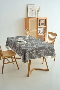 Detail of grey rectangular tablecloth featuring white floral print and tassel edges