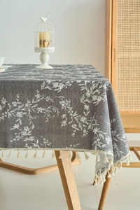 Detailed view of grey linen tablecloth with white floral patterns and tassel edge decor