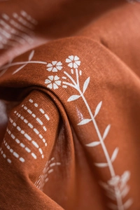 Gros plan du tissu en lin orange montrant des imprimés floraux blancs et la texture
