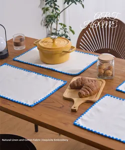 Detail of embroidered linen placemat with blue wavy scalloped edge on wooden table