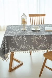 Detail of grey rectangular tablecloth with white floral patterns and cream fringe tassels