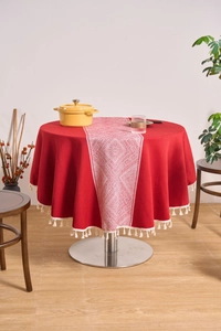 Detail of red cotton linen round tablecloth featuring white geometric runner and tassels