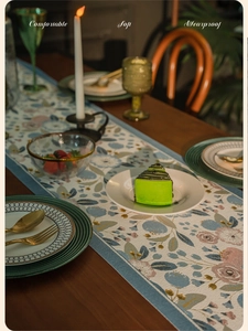 Detail of floral jacquard table runner with fringe tassels on a wooden table setup