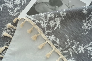 Close-up of gray floral tablecloth with cotton linen texture and cream fringe tassels