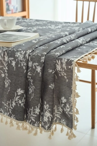 Detailed view of dark grey tablecloth with white floral prints and beige tassel trim edge