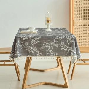 Gray rectangular tablecloth with white floral print and tassel edges on a wooden table