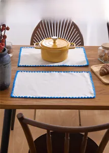 Detail of rectangular cream linen placemats with blue crochet borders on a wood table