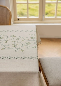 Close-up of rectangle linen tablecloth featuring green leaf embroidery and fringe edges