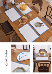 Detail of white dining placemat with blue shell pattern embroidery and scalloped edges
