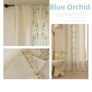 Détail de la broderie orchidée cyan et des pompons raffinés sur des rideaux en lin beige
