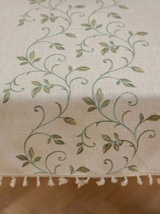 Detail of linen tablecloth featuring green vine embroidery and elegant cotton tassels