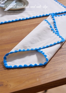 Detail of white cotton linen placemat with blue scalloped embroidery on a wooden table