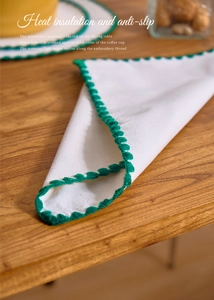 Detail of white cotton placemat featuring green scalloped embroidered edges on wood table