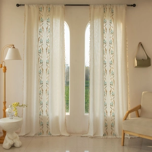 Détail du rideau en lin crème avec broderies de fleurs bleues et pompons blancs