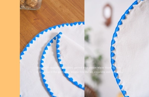 Macro detail of creamy white placemat featuring blue scalloped edge embroidery on wood table