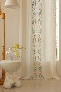 Détail de la broderie florale et des franges sur des rideaux en lin semi-transparents