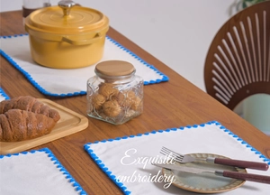 Close-up of white cotton placemat with blue scalloped embroidery on a wooden table