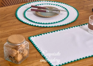 Detailed embroidery on white fabric placemats with green wavy stitched edges