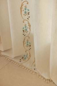 Détail de fleurs bleues brodées sur des rideaux en lin beige avec franges