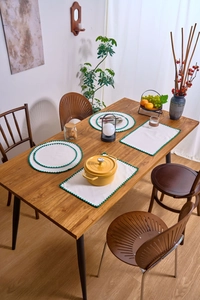 Detail of minimalist cream placemats with green wavy embroidery on a wooden table