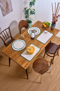 Top view of cream embroidered placemats with green wavy edges on a wooden dining table