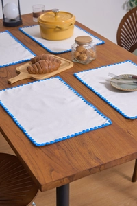 Close-up of four white linen place mats with blue scalloped edges on a wooden table