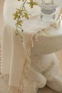 Gros plan sur un tissu crème texturé avec bordures à franges sur un tabouret en pierre