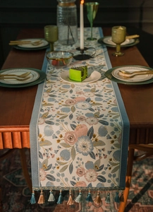 Macro view of floral jacquard table runner with decorative colorful tassels on wooden table
