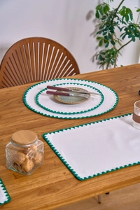 Detail of white embroidered placemat with green scalloped edges for dining table