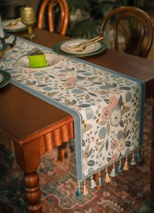 Detail of floral jacquard table runner featuring blue fringe tassels on wooden table surface
