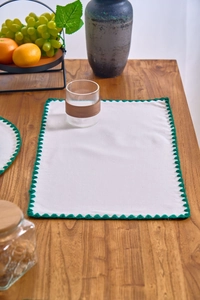 Close-up of white fabric placemats with green crochet scalloped edges on a wooden table