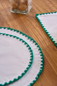 Close-up of white linen placemats with green crochet triangle border on wood table