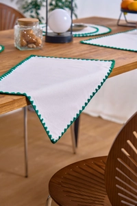 Close-up of white cotton linen placemat with green scalloped embroidery on wood table