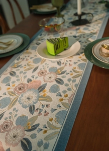 Detail of floral jacquard table runner with fringe on a wooden dining table