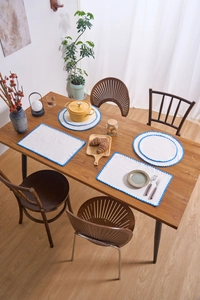 Close-up of beige fabric placemats with blue scalloped embroidery on a wooden table