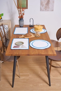 Detailed close-up of white fabric placemats with blue crochet wavy edges on a wooden table