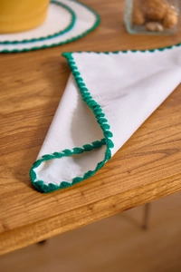 Detailed view of white linen napkin with green crochet lace border on wooden surface