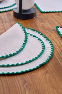 Detail of white cotton linen placemat with green crochet embroidery and scalloped edges