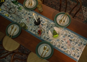 Close-up of vintage floral jacquard table runner with blue tassels on a wooden table