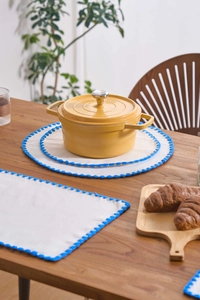 Detail of white cotton placemat with blue scalloped embroidery on a wooden table