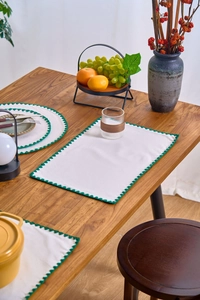 Detail of embroidered placemat with green sawtooth border on a wooden table setup