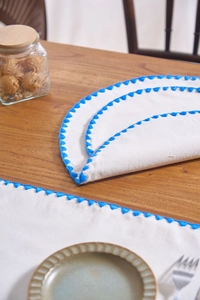 Detailed view of white cotton placemat with elegant blue scalloped embroidered edge