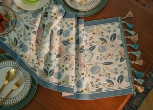Close-up of floral jacquard table runner with blue tassels on a dark wooden table