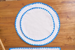 Macro shot of white round cotton placemats with vibrant blue scalloped embroidered edges