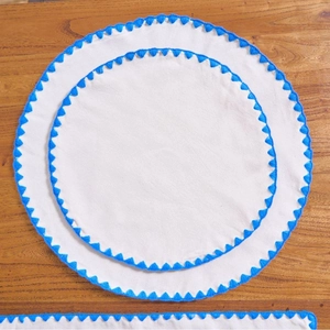 Modern white fabric round placemat with blue crochet lace trim on a wood table