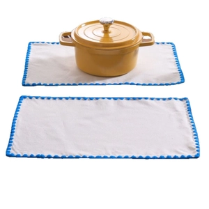 Minimalist cream fabric placemat set with blue pom-pom fringe and yellow cast iron pot