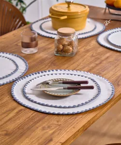 Detail of round cream placemat with navy blue embroidery on a wooden table surface