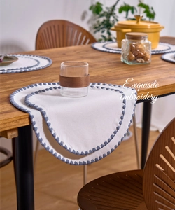Detail of white cotton linen placemat featuring blue embroidery on a wooden table