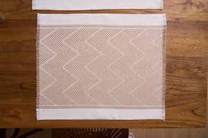 Detail view of woven placemat with geometric patterns and fringe on wooden table